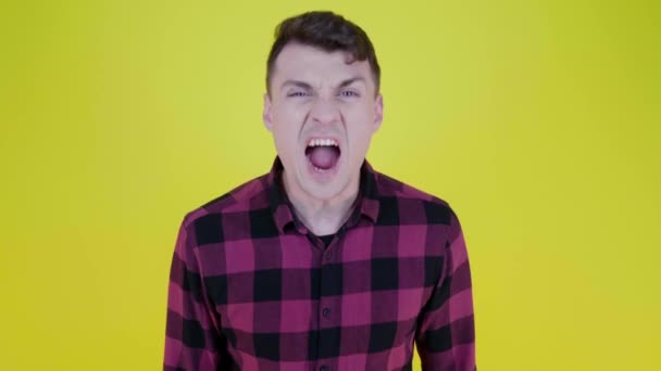 Boze man in een roze geruite shirt schreeuwt in de camera op een gele achtergrond — Stockvideo