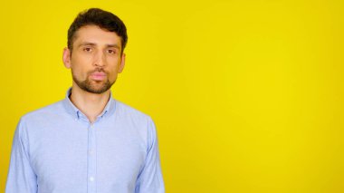 Sarı arka planda açık mavi gömlekli sakallı adam.