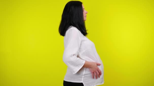 Junge schwangere Frau massiert Bauch mit den Händen auf gelbem Hintergrund — Stockvideo