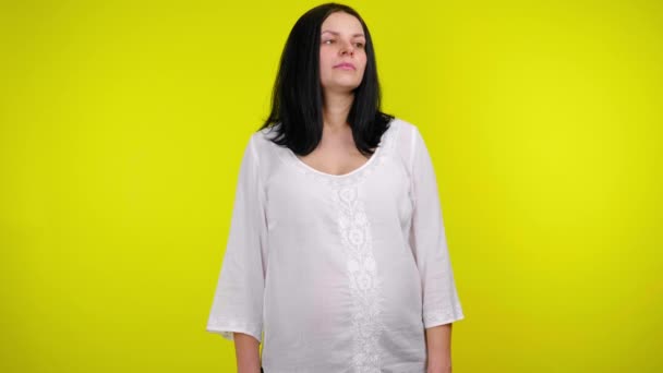 Молода вагітна жінка в білій блузці дивиться навколо на жовтому тлі — стокове відео