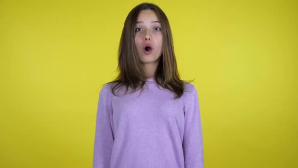 Tiener meisje in een roze trui is geschokt op gele achtergrond met kopieerruimte — Stockvideo