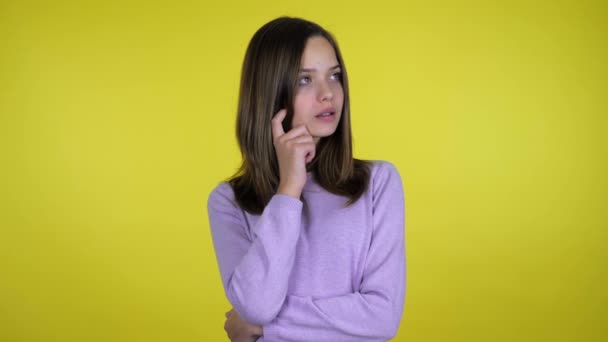 Menina adolescente com um dedo na bochecha olha em volta e pensa o que escolher — Vídeo de Stock