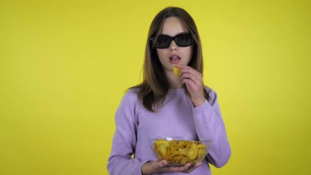 Meisje kijkt film in zwart 3D bril, eet chips, glimlacht en wijst vinger — Stockvideo