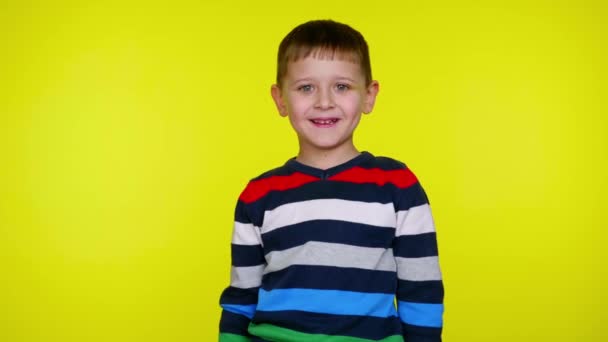 Cheerful little child boy smiles and looks at the camera on a yellow background — Stock Video