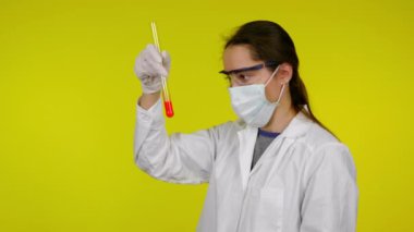 Beyaz elbiseli kadın, koruyucu maske test tüpünün içindekileri inceliyor.