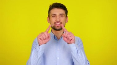 Sweet young man in light blue shirt draws a heart in the air with his fingers