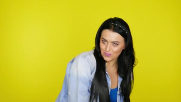 Жінка з чорним волоссям в джинсовій куртці танцює на жовтому тлі — стокове відео