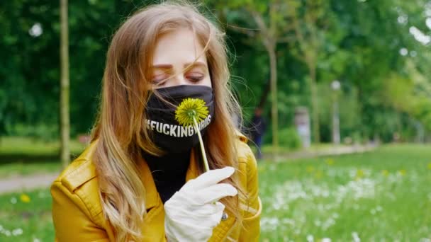 Vrouw met een zwart masker en witte latex handschoenen ruikt gele bloem door een masker — Stockvideo