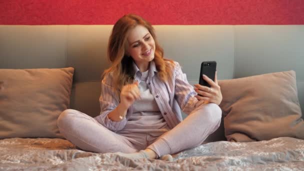 Femme tenant un smartphone dans sa main, saluant et parlant par vidéo, souriant — Video