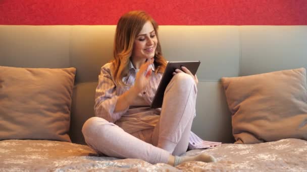 Femme gaie avec une tablette à la main, parle à un ami par appel vidéo, souriant — Video