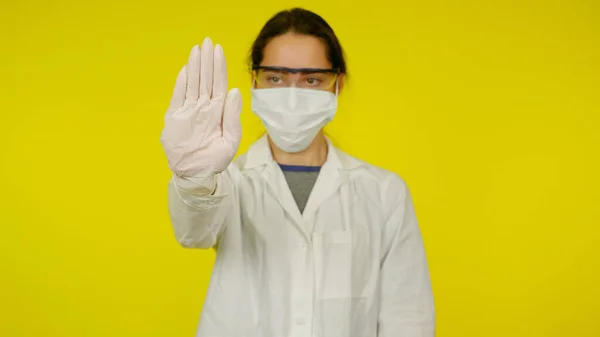 Ung läkare i en medicinsk mask, skyddsglasögon och latexhandskar visar ett stopp med handen — Stockfoto