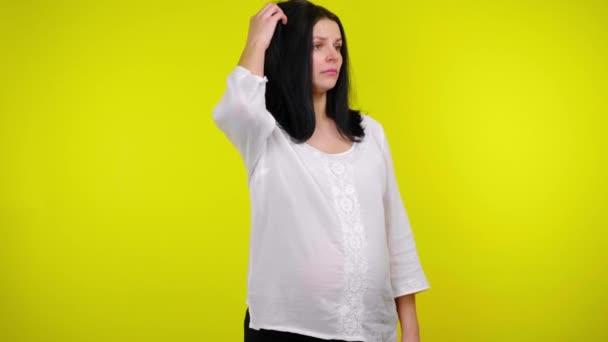 Düşünceli hamile kadın etrafına bakıyor, sarı arka planda ne seçeceğini düşünüyor. — Stok video