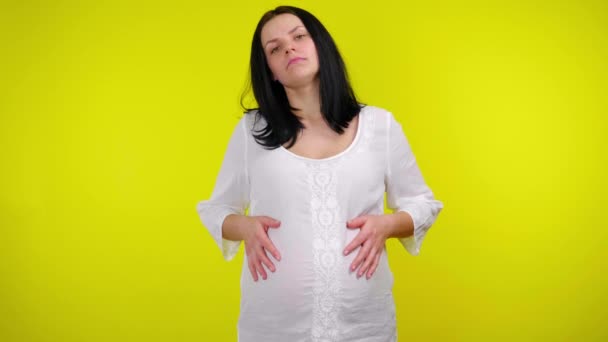 Усталая беременная женщина с черными волосами в белой блузке массирует живот руками — стоковое видео