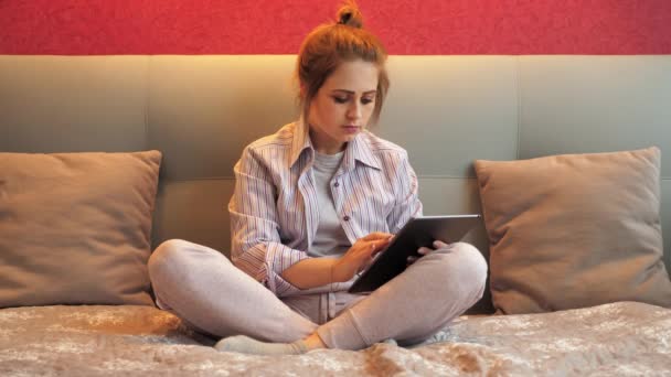 Femme fatiguée assise sur le lit utilise la tablette pour le travail, bâille et s'endort — Video