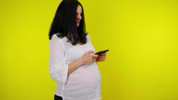 Une jeune femme enceinte positive tient un smartphone dans les mains et joue au jeu vidéo — Video