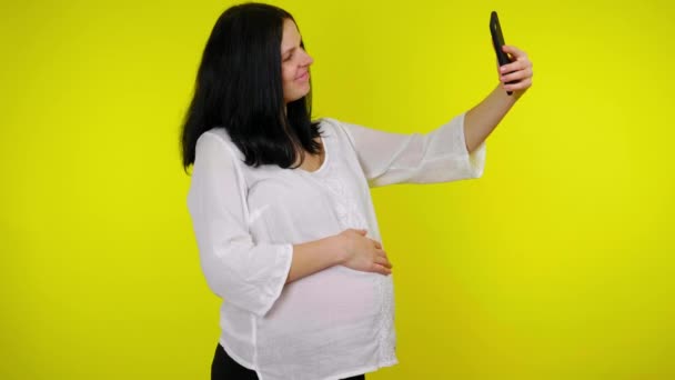 Ciężarna kobieta nagrywa wideo na smartfonie selfie aparat, pokazuje brzuch rodziców — Wideo stockowe