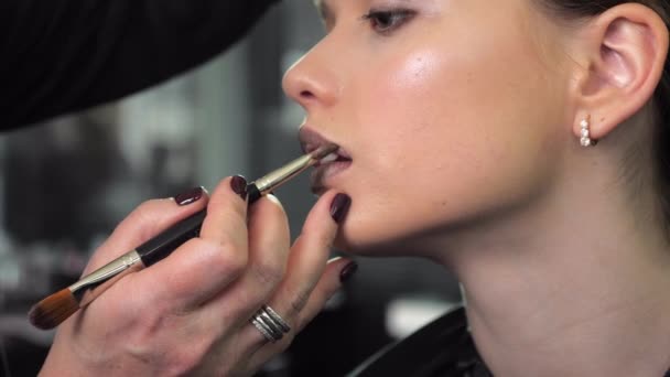 Makeup artist applica il rossetto sulle labbra utilizzando pennello per una ragazza adolescente in un salone — Video Stock