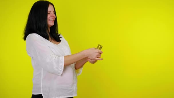 Lycklig gravid kvinna exploderar konfetti kanon och ler på en gul bakgrund — Stockvideo