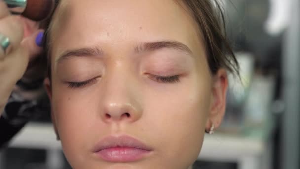 Make-up umělec aplikuje základ na tvář se štětcem na dospívající dívku v salonu — Stock video