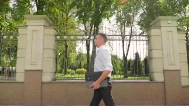 Elinde dizüstü bilgisayarı olan bir iş adamı parkta yürüyor.