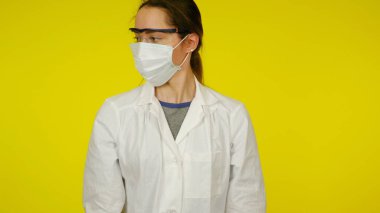 Koruyucu tıbbi maskeli, gözlüklü ve beyaz önlüklü genç bir doktor.