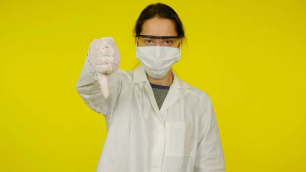 Young doctor in protective medical mask, glasses, latex gloves shows dislike