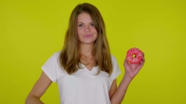 Beyaz tişörtlü bir kadın donutla el kaldırıyor, hoşnutsuzluk ve somurtkanlık gösteriyor.