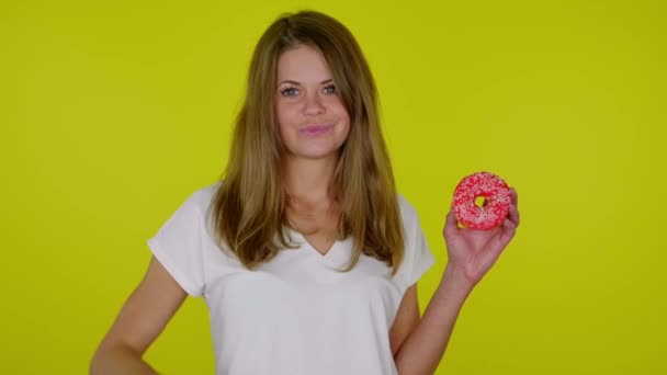 Beyaz tişörtlü bir kadın donutla el kaldırıyor, hoşnutsuzluk ve somurtkanlık gösteriyor. — Stok video