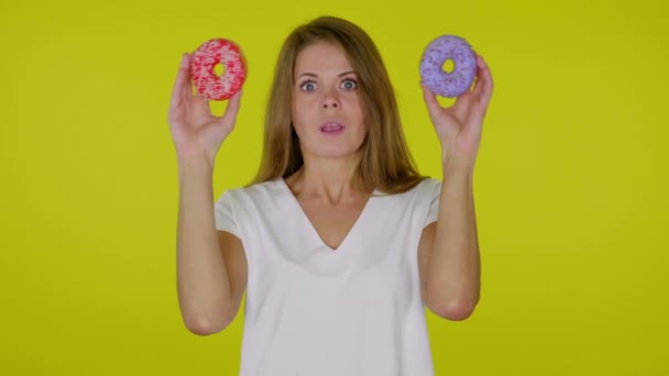 Vrouw neemt handen van ogen met blauwe en rode donuts, geschokt, verrast — Stockvideo