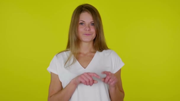 Женщина улыбается и рисует сердце в воздухе с пальцами на желтом фоне — стоковое видео
