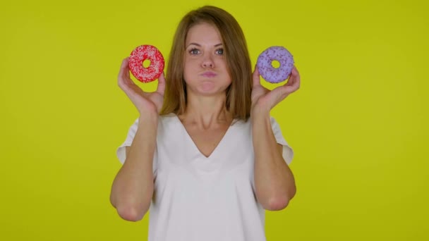 Mulher olha para um delicioso azul, rosquinhas vermelhas nas mãos com bochechas, boca — Vídeo de Stock