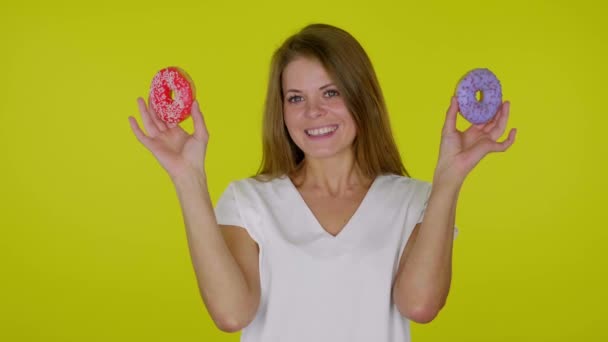 Woman smiles, takes hands from eyes with blue, red donuts on a yellow background — Stock Video