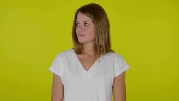 Uma mulher animada em uma camiseta morde o lábio, olha em volta e pensa o que escolher — Vídeo de Stock