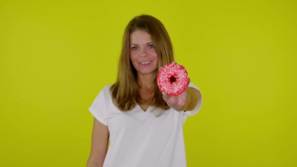 Mulher morena positiva levanta a mão com um donuts vermelho na câmera e sorri — Vídeo de Stock