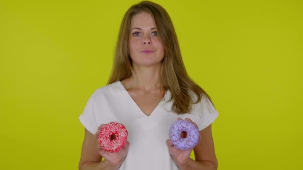 Brunette vrouw in een wit T-shirt wervelt blauw en rood donuts op de borst en glimlacht — Stockvideo