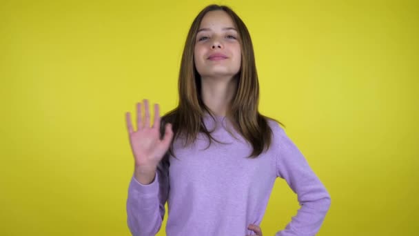 Hallo oder Tschüss. Teenager-Mädchen lächelt und schüttelt ihre Hand auf gelbem Hintergrund — Stockvideo