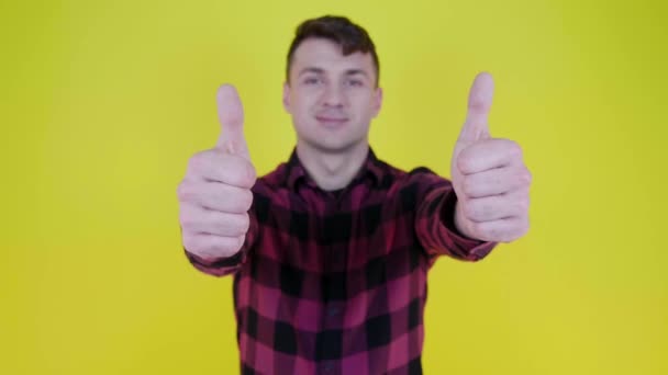 Man in pink plaid shirt smiles, raises hand and shows like on yellow background — Stok Video