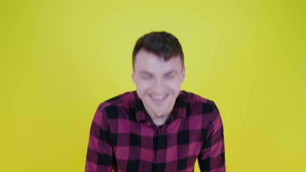 Hombre con una camisa a cuadros rosa mira a la cámara y se ríe sobre un fondo amarillo — Vídeos de Stock