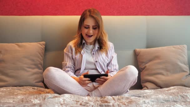Kvinna spelar ett TV-spel på en smartphone, vinner, gläds åt segern och ler — Stockvideo