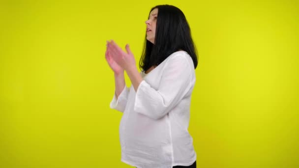 Mulher grávida jovem doente em uma blusa branca espirra em um fundo amarelo — Vídeo de Stock