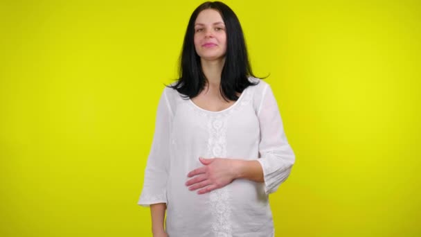 Mulher grávida feliz segura a mão em seu estômago, mostra como e sorri — Vídeo de Stock