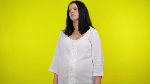 Mujer embarazada pensativa mira a su alrededor, piensa qué elegir en el fondo amarillo — Vídeos de Stock