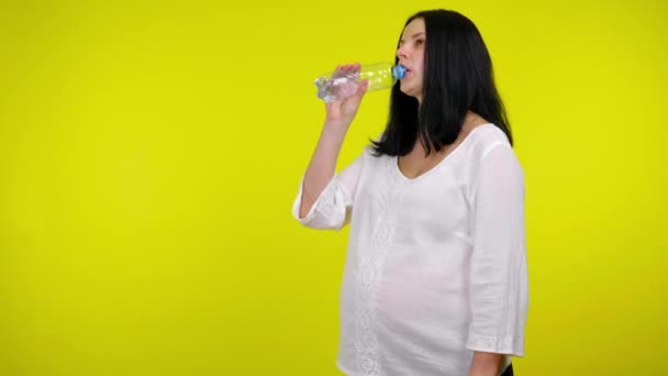 Ung gravid kvinna dricker vatten i en plastflaska på en gul bakgrund — Stockvideo