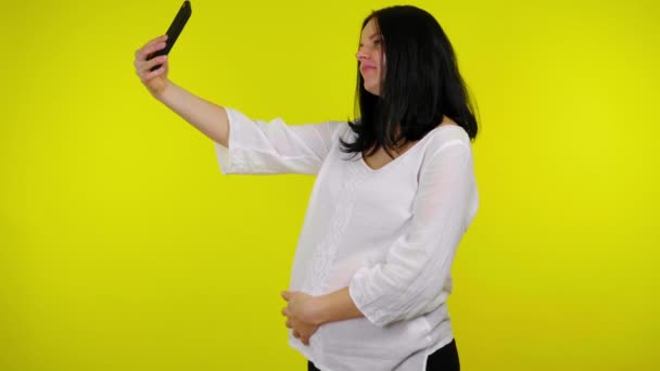 Giovane donna incinta scatta foto selfie con uno smartphone su uno sfondo giallo — Video Stock