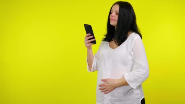 Positive jeune femme enceinte utilise smartphone et tient son ventre avec sa main — Video