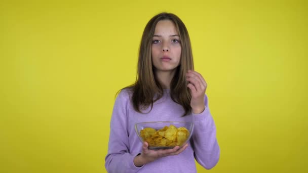 ティーネージャー女の子食べるポテトチップスとともにガラスボウル上の黄色の背景 — ストック動画