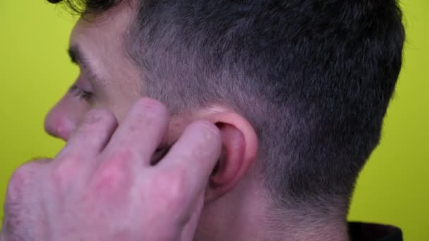 El hombre de cerca inserta un auricular inalámbrico blanco en la oreja sobre un fondo amarillo — Vídeo de stock