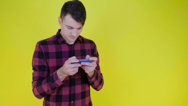 El hombre juega con entusiasmo el videojuego en un teléfono inteligente sobre un fondo amarillo — Vídeo de stock