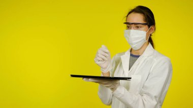 Tıbbi maskeli, gözlüklü ve lateks eldivenli doktor elinde bir tablet tutuyor.