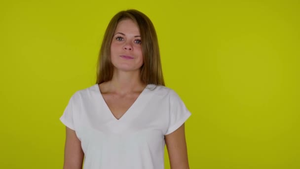 Mujer con una camiseta blanca se gira hacia la cámara y sonríe sobre un fondo amarillo — Vídeos de Stock